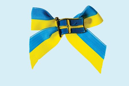 Close up macro view of metal badge in form of swedish flag on blue yellow bow isolate in blue background.の写真素材