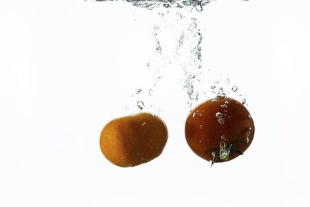 Close up view splashing water and red tomato and mandarin on white background. Beautiful backgrounds.の写真素材