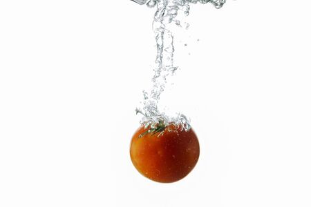 Close up view splashing water and red tomato on white background. Beautiful backgrounds.の写真素材