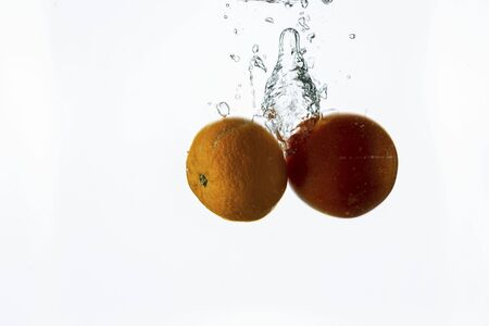 Close up view splashing water and red tomato and mandarin on white background. Beautiful backgrounds.の写真素材