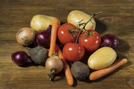 Close up view of colorful vegetables isolated on wooden background. Potatoes, tomatoes, yellow and red onion, carrot, beetroot.の写真素材