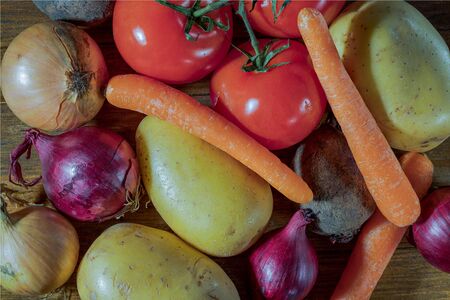 Close up view of colorful vegetables isolated on wooden background. Potatoes, tomatoes, yellow and red onion, carrot, beetroot.の写真素材