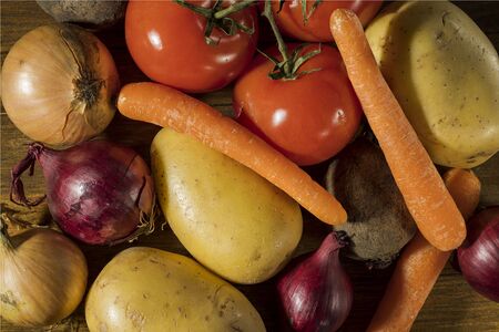 Close up view of colorful vegetables isolated on wooden background. Potatoes, tomatoes, yellow and red onion, carrot, beetroot.の写真素材