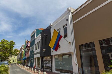 Beautiful landscape view of central street of city Willemstad, Curacao. Colorful buildings Embassy of Colombia and green trees on blue sky with white clouds background.の写真素材