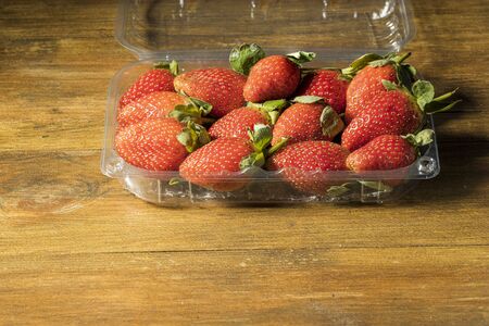 Close up view of strawberries in plastic container isolated on wooden background.の写真素材