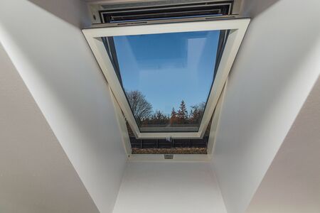 Close up view of open roof window isolated with view of trees on blue sky background.の写真素材