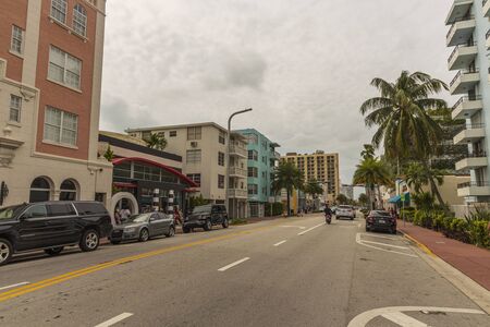 Beautiful landscape view of street of Miami Beach. White buildings and palm trees on both sides of asphalt road on blue sky and white clouds background. USA Miami South Beach. 22/09/2019.のeditorial素材