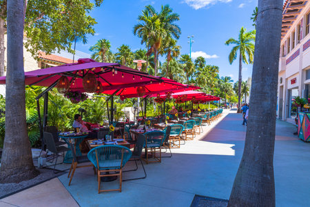 Beautiful landscape view of outdoor cafe. Blue chairs under red umbrellas on green trees and blue...
