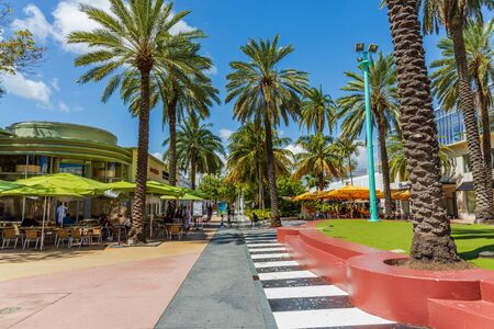 Beautiful view of outdoor cafe on one of Miami South Beach. Beautiful buildings and green trees on background. Eating out concept. Tourism concept. USA Miami South Beach. 24/09/2019.のeditorial素材