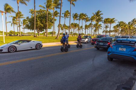 View of tourists driving on segways on beautiful summer day. Road and green palm trees on blue sky background. USA Miami South Beach. 24/09/2019.のeditorial素材