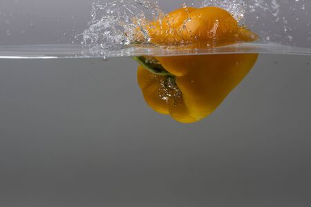 Close up view splashing water and falling yellow pepper. Beautiful backgrounds.の写真素材