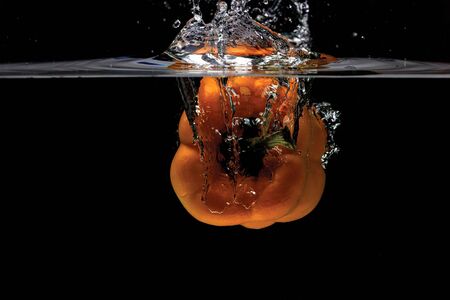 Close up view of colorful yellow pepper falling in water on black background. Gorgeous backgrounds.の写真素材