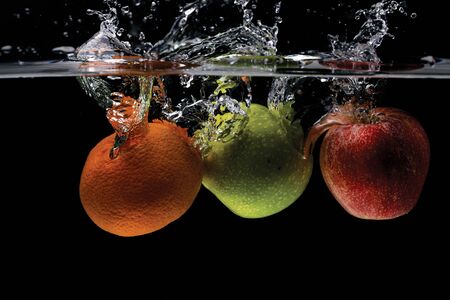 Close up view of colorful fruits falling in water on black background. Gorgeous backgrounds.の写真素材
