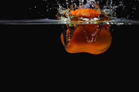 Close up view of colorful yellow pepper falling in water on black background. Gorgeous backgrounds.の写真素材