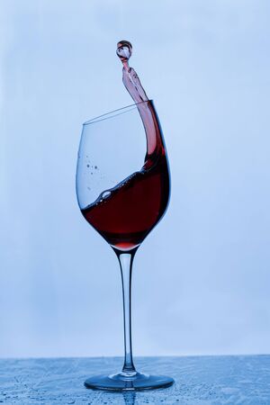 Close up view of splashing red wine in glass isolated on blue background.の写真素材