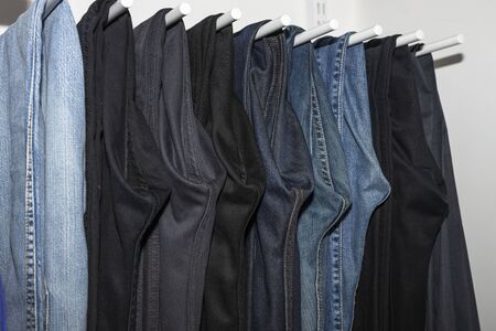 Close up view of interior of built-in wardrobe. Blue and black jeans on white hangers. Cloth organizer.の写真素材
