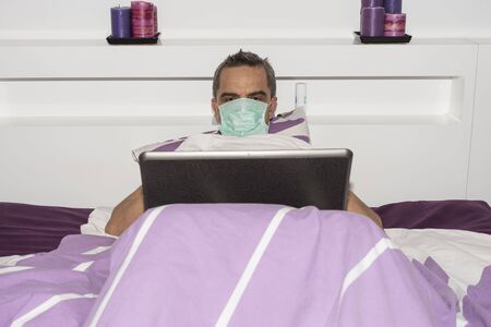 View of male in mouth mask laying in bed. COVID 19. Health concept.の写真素材
