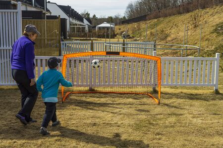 Stay at home. Outdoor games. Grandma with grandson playing football on backyard. Covid-19.の写真素材