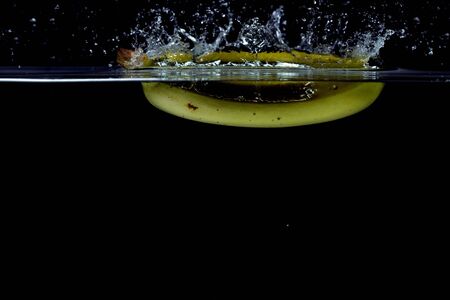 Close up view of colorful banana falling in water on black background. Gorgeous backgrounds.の写真素材
