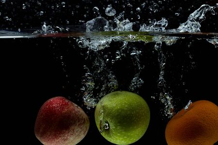 View of colorful fruits falling in water on black background. Gorgeous backgrounds.の写真素材