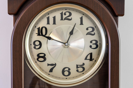 Close up macro view of brown clock with light clock face showing almost twelve fifty o'clock. Time...