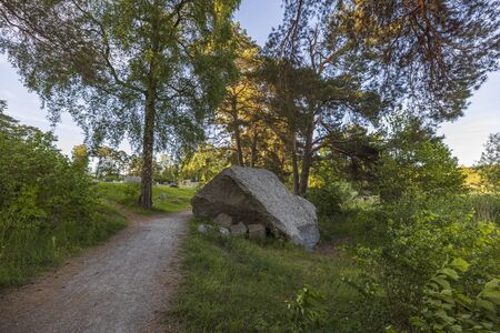 Beautiful big rock of strange natural form near path in forest. Big tall trees and blue sky on background. Sweden Europeの写真素材