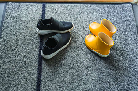 Close up view of yellow and black pair summer kid shoes on mat near entrance door. Kid shoes concept.の写真素材