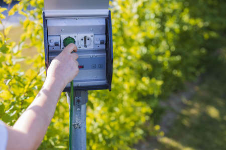 Close up view of female hand connecting cable to outdoor power outlet. Technology concept.の写真素材