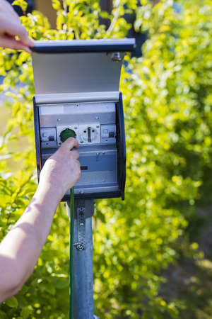 View of female hand connecting cable to outdoor power outlet. Technology concept.の写真素材