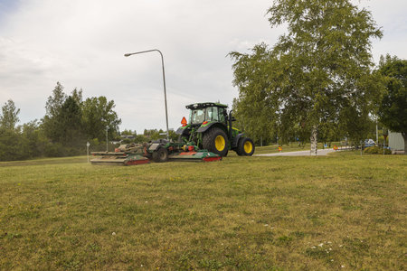 Beautiful view of worker on modern lawn mower machine taking care of town grass field.