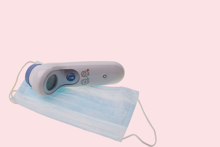 Close up view of face mask and kind of thermometer isolated on pink background. Covid-19. Health...