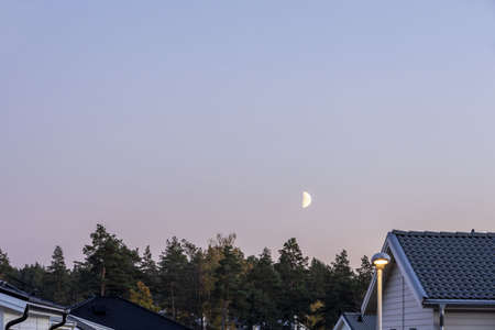 Gorgeous landscape view. Early crescent moon in evening sky over hose roofs.の写真素材