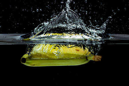 Close up view of colorful yellow banana falling in water on black background.の写真素材