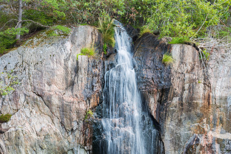 Gorgeous natural landscape view. Small waterfall on rocky landscape and green plants on background....