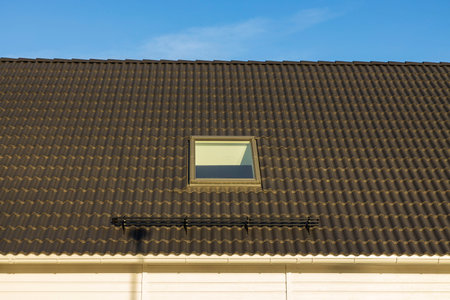 Close up view of dormer roof window. Brown tile roof on blue sky background