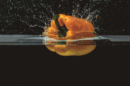 Close up view of colorful yellow pepper falling in water on black backgroundの写真素材