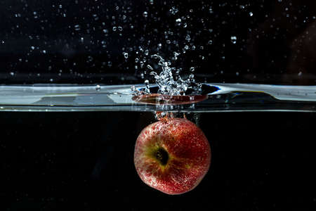 Close up view of colorful apple falling in water on black background. Gorgeous backgrounds.の写真素材