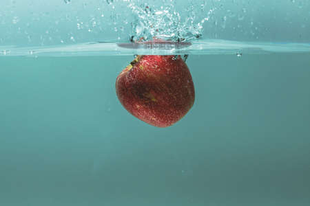 Close up view of colorful apple falling in water on turquoise background. Gorgeous backgrounds.の写真素材