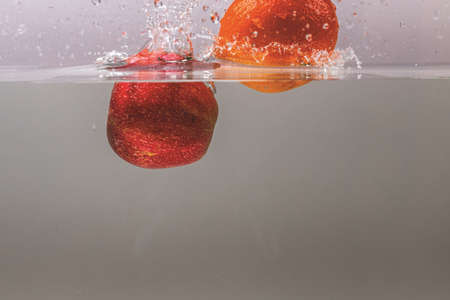 Close up view of colorful fruits falling in water on gray background. Gorgeous backgrounds.の写真素材