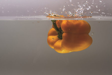 Close up view of colorful yellow pepper falling in water on background.
