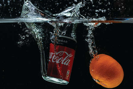 Close up view of cans of Coca Cola and mandarin falling into water with spray. Sweden. Uppsala. 03.25.2021.のeditorial素材