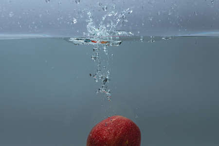 Close up view of colorful apple falling in water on blue background. Gorgeous backgrounds.の写真素材