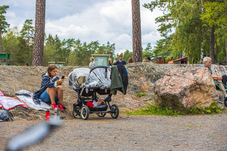 View of young woman sitting near baby sleeping in baby carriage in park. Kolmorden, Sweden. 09.28.2020.のeditorial素材