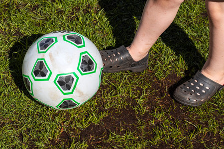 Close up view of the child's feet near ball on grass lawn background. Sweden.