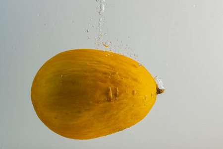 Close up view of yellow melon falling in water on gray background. Gorgeous backgrounds.の写真素材
