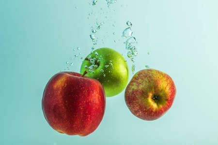 Close up view of colorful apples falling in water on turquoise background. Gorgeous backgrounds.の写真素材