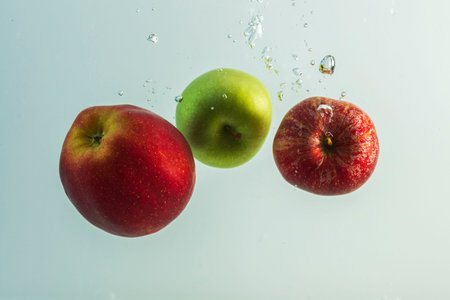 Close up view of colorful apples falling in water on turquoise background. Gorgeous backgrounds.の写真素材
