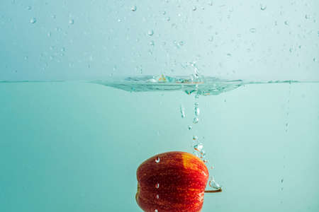 Close up view of colorful apple falling in water on turquoise background. Gorgeous backgrounds.の写真素材