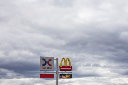 View of logotype board of well-known gas station OKQ8 and McDonald's logotype board on white clouds...