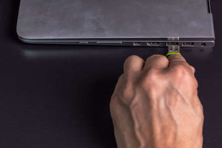 View of man hand connecting usb flash drive to silver notebook computer isolated on black background. Sweden.の写真素材